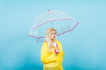 忧郁无聊的金发女人，穿着黄色雨衣，撑着透明的雨伞等雨。忧伤无聊的女人穿着雨衣撑着伞