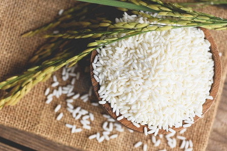 吃东西摄影照片_茉莉花白米在木碗里和收获黄撕裂稻米在袋子上，收获大米和粮食烹饪概念