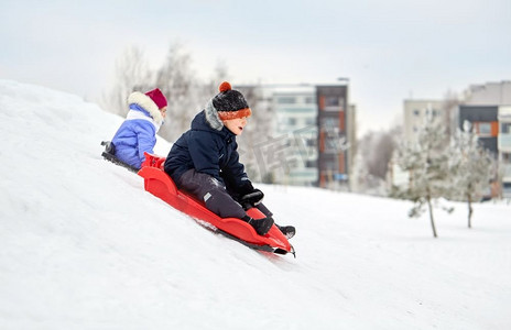 圣诞孩子们摄影照片_童年，雪橇和季节概念—快乐的小孩子在冬天滑下雪山的雪橇。冬天，孩子们在雪橇上滑下雪山