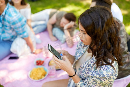 休闲、科技和人的概念-女性在夏令营与朋友野餐时使用智能手机。与朋友野餐时使用智能手机的女性
