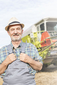 自信的高级农民站在农场的拖拉机的肖像