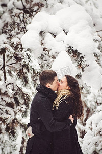 下雪保暖摄影照片_一男一女穿着保暖的衣服，戴着围巾，在雪林和田野中散步