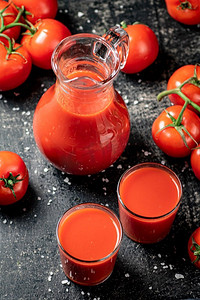 桌子上有一只盛有番茄汁的水壶。在黑色背景上。高质量的照片。桌子上有一只盛有番茄汁的水壶。