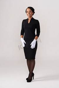 穿黑裙子戴白手套的空姐。微笑的非洲妇女空姐在灰色背景乘务员肖像