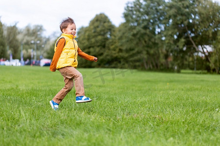 童年、休闲和人的概念-快乐的小男孩在公园的绿地上跑步。快乐的小男孩在公园里跑步