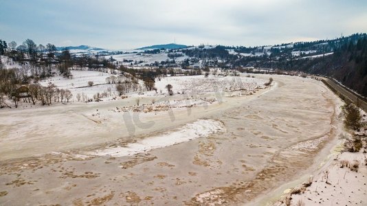 村路摄影照片_冰冻的冬天河。雪村和道路的空中乡村视图。早春融化的冰雪。