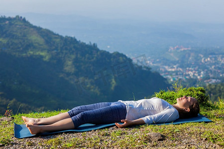 挺尸式摄影照片_妇女放松瑜伽asana Savasana—尸体姿势户外在喜马拉雅山。印度喜马偕尔邦。妇女放松在瑜伽asana Savasana户外