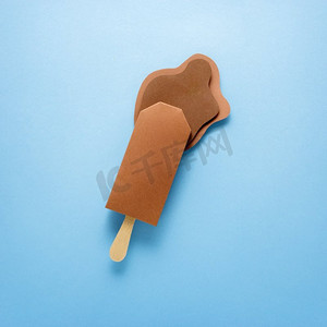 创意概念照片冰淇淋冰棒和飞溅由纸制成在蓝色背景。