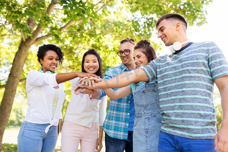人，友谊，国际概念--一群快乐的微笑的朋友在公园里堆积着手。开心的微笑的朋友在公园里握手