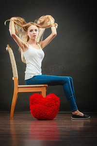 心碎的爱情观。悲伤忧郁的女人坐在椅子上，地板上的红心枕头，黑暗的背景