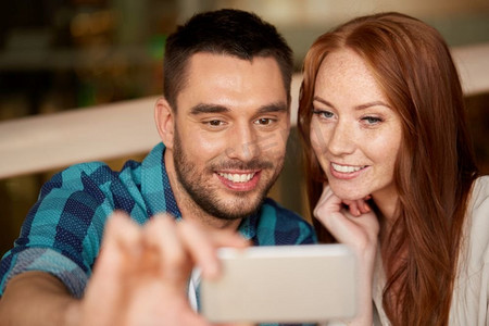 休闲、科技和人的概念-幸福的情侣在餐厅用智能手机自拍。一对情侣在餐厅用智能手机自拍