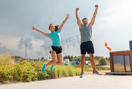健身，运动和生活方式的概念—快乐的夫妇在运动衣服跳海滩。快乐的夫妇在运动衣服跳跃在海滩