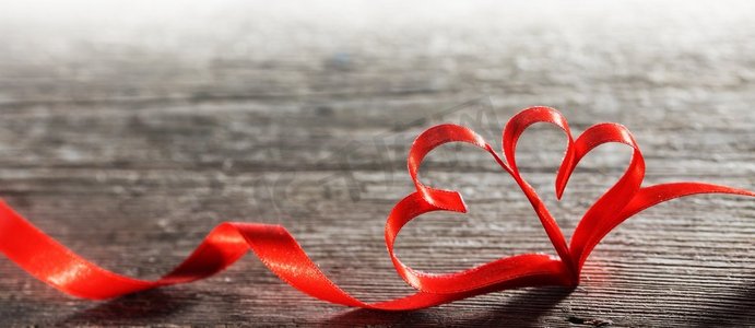 木质背景上有两颗红丝带心形图案，情人节概念。木头上的两颗丝带心