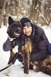 一名穿着夹克、戴着针织帽的男子带着一只美国秋田狗穿过雪地森林