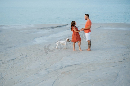 年轻夫妇橙色衣服与狗在空沙滩
