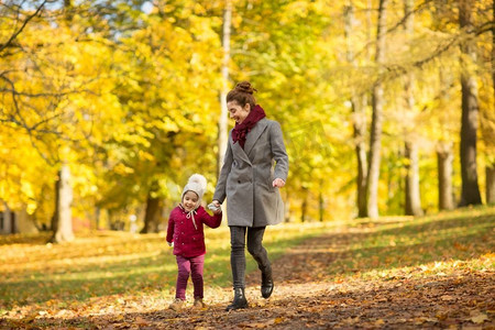 家、季节、人的概念-快乐的母女漫步在秋天的公园里。秋天公园里快乐的母亲和小女儿