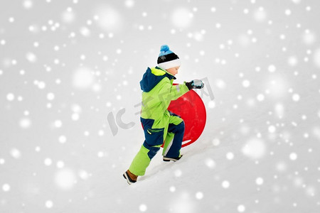 冬天小男孩摄影照片_童年、雪橇和季节概念-冬天带着雪碟在户外滑雪的快乐小男孩。冬天用雪碟拉雪橇的快乐男孩