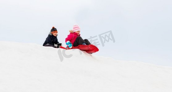 小孩子摄影照片_童年，雪橇和季节概念—快乐的小孩子在冬天滑下雪山的雪橇。快乐的孩子们滑在雪橇下山在冬天