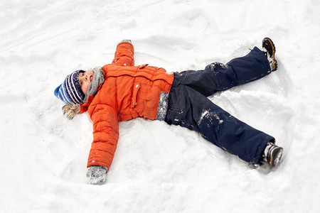 童年、休闲和季节概念--快乐的小男孩穿着冬衣在户外堆雪天使。快乐的小男孩在冬天堆雪天使