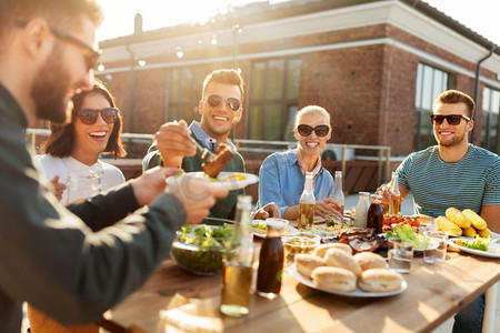 休闲与人际概念—快乐的朋友在天台烧烤聚会上吃喝。朋友在屋顶吃晚餐或烧烤派对
