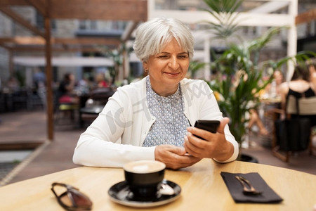 技术，老年和人的概念—愉快的高级妇女与智能手机在街道咖啡馆。快乐的高级妇女与智能手机在街头咖啡馆