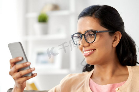 印度女性摄影照片_人与科技概念--快乐的印度女性在家使用智能手机。快乐的印度女人在家使用智能手机