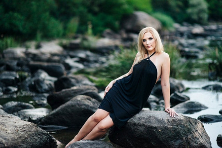 黑裙子摄影照片_石质河岸上一位穿着黑裙子、蓝眼睛的金发女孩