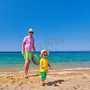 两岁的蹒跚学步的男孩在海滩上与父亲走，拿着充气戒指。暑假家庭度假。希腊，西托尼亚。 