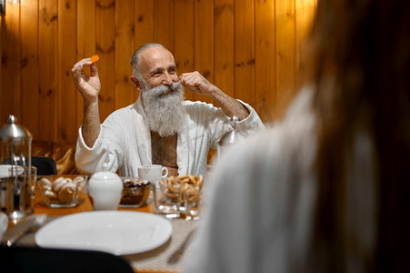 坐在餐桌旁的老人在桑拿浴室休息时与年轻女子调情.人物特写指挥大师