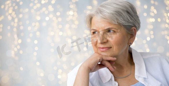 年龄和人概念—沉思的高级妇女肖像在节日光背景。节日灯光下的老年妇女肖像