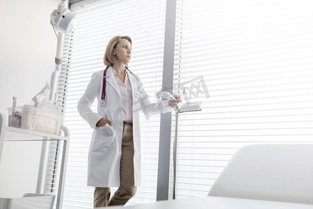 富有说服力的成熟医生站在测量规模，而通过窗口看在医院