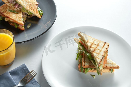 两个俱乐部三明治，各种馅料和橙汁放在桌子上。两个俱乐部三明治与各种馅料