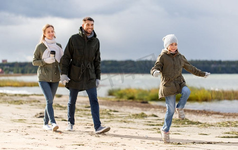 家庭，休闲和人的概念—快乐的母亲，父亲和小女儿沿着秋天的海滩散步。快乐的家庭漫步在秋天的海滩