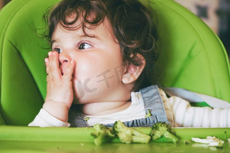 婴儿吃食物在她的绿色高脚椅