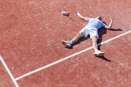 竞争性摄影照片_夏天，失望的成年男子全身躺在球场上的网球拍旁