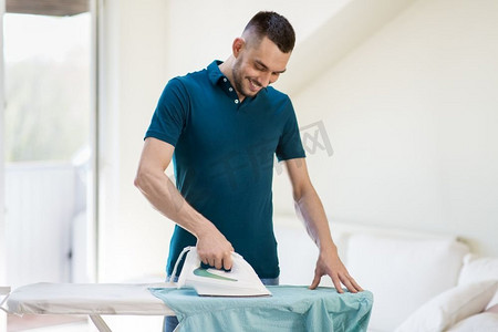 家务和家庭概念—男人在家里熨衬衫。男人在家里用熨斗熨衬衫