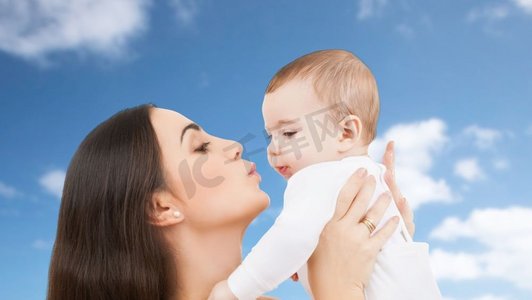 家庭和母性概念-快乐微笑的年轻母亲在天空中亲吻小婴儿的背景。母亲在天空中亲吻婴儿的背景