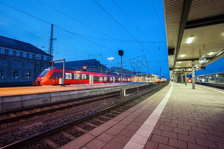 德国纽伦堡的现代化火车站，夜间铁路上有客运列车。快速的红色通勤列车..工业景观