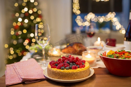 圣诞晚餐摄影照片_圣诞晚餐和吃概念—浆果蛋糕和其他食物在家里的餐桌上。在家里的圣诞餐桌上的蛋糕和其他食物