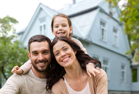 家庭，房地产和住宿概念—快乐的母亲，父亲和小女儿在房子的背景。快乐的家庭在房子背景