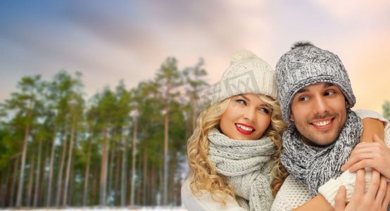 冬天、圣诞节和人们概念快乐的情侣戴着帽子和围巾在森林上空拥抱。一对情侣在冬日森林的背景下拥抱