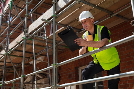 男性建筑工头、建筑工人或工地经理手持写字板，穿着白色安全帽和透明背心