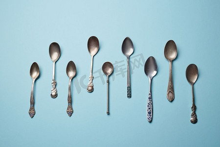 不锈钢小勺子摄影照片_收集不同的复古金属汤匙上的蓝色纸张背景俯视图。不锈钢小厨房甜点勺子，蓝色隔绝