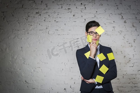 体贴的女商人，脸上贴着空白的黄色粘贴纸，办公室里穿着靠墙的西装