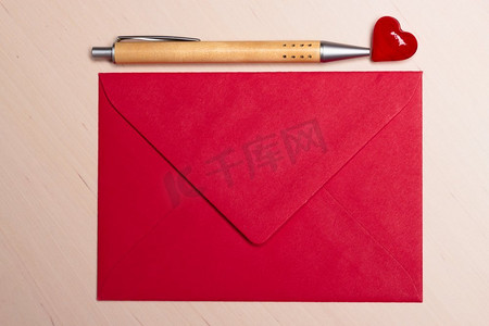 小心讨好摄影照片_红色空白信封小心和笔在木表面。情人节卡片，爱情或婚礼问候概念。