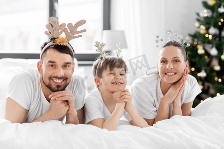 寒假班单页摄影照片_家庭、寒假和人们的概念-圣诞节早晨快乐的父母和小儿子在床上。圣诞节早晨，一家人躺在床上
