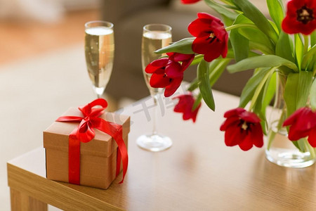 邀请函香槟色摄影照片_情人节和浪漫的概念—礼品盒，香槟杯和鲜花在桌子上。礼品盒，香槟杯和鲜花在桌子上