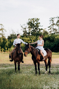 一个女孩在一个白色背心裙和一个男人在一个白色衬衫散步与棕色的马在村庄