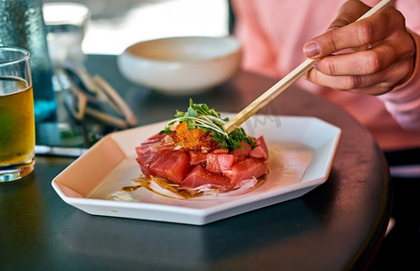妇女吃新鲜的生金枪鱼菜，夏威夷当地食物戳，在户外餐厅餐桌。夏威夷戳碗食物盘。