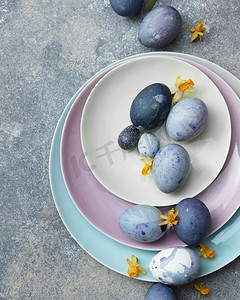 板蓝花摄影照片_复活节蓝蛋在一个彩色的餐盘与花在石头背景。蓝色复活节彩蛋。